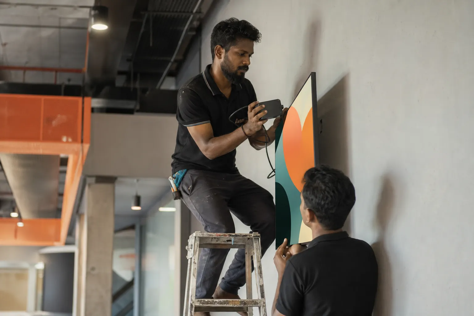 An engineer installing a media player behind a wall-mounted screen in an industrial building