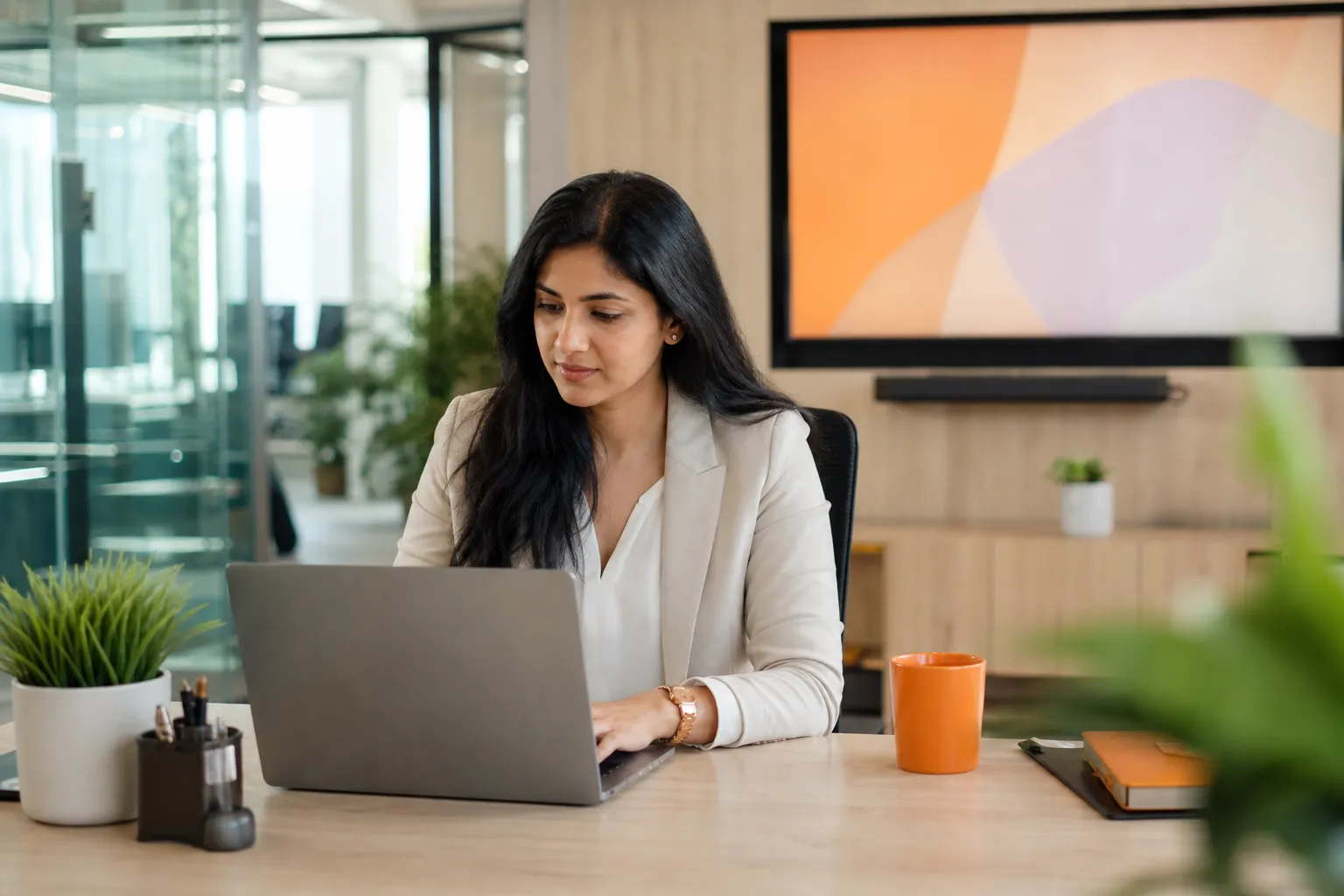 An HR manager reviewing a notice on a laptop beside a wall screen showing a company announcement
